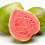 Due frutti di guava interi con buccia verde e una metà tagliata che mostra la polpa rosa brillante e i semi, isolati su sfondo bianco.